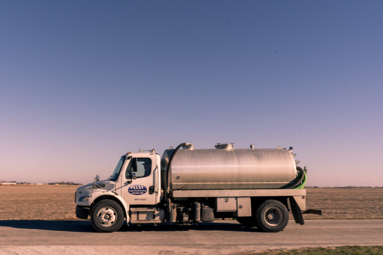 Pelsy septic pump truck on a county road beside a harvested field